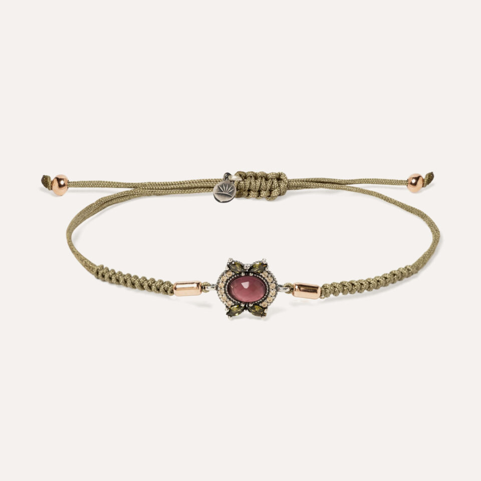 El cabujón central es una turmalina rosa facetada de 5×7 mm, acompañada de 4 circonitas talla marquise color verde peridoto de 2,5x4mm, y rodeada de circonitas color cava de 1,25 mm clavadas a mano